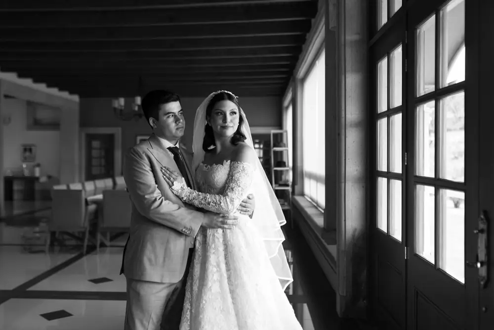 Retrato en blanco y negro de los novios abrazados junto a la ventana