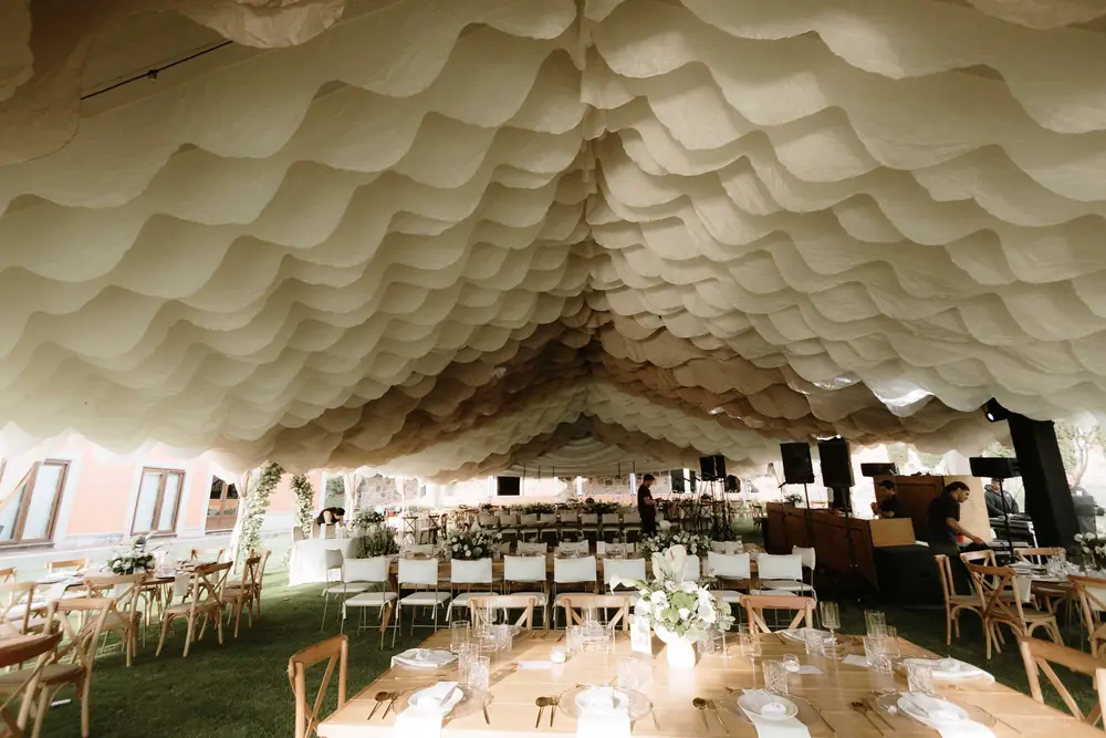 Toldo con techo de tela en ondas y mesas largas de madera